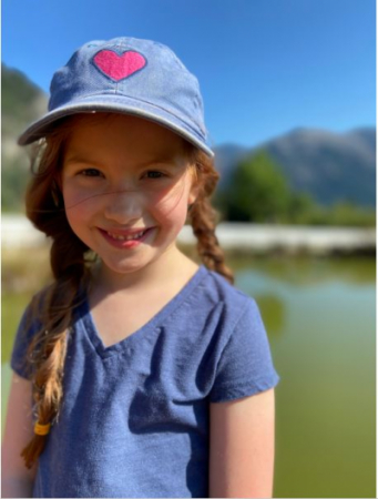 Little girl with a purple hat and shirt smiling in the sun