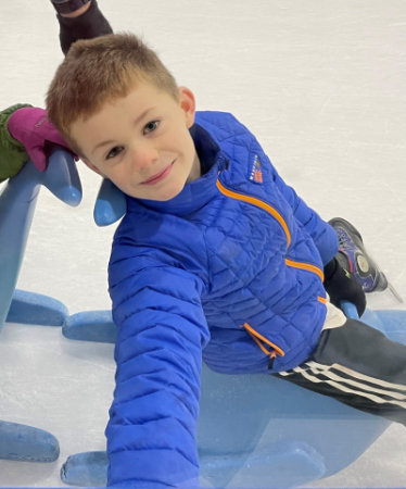 A boy in a blue jacket sitting on a sled in an ice rink