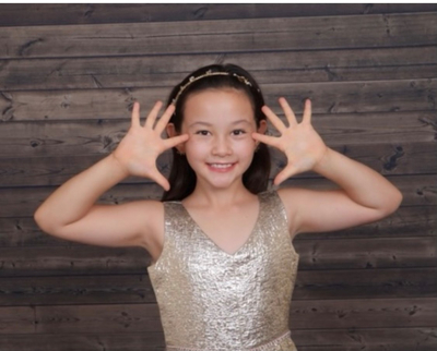 A smiling girl in a sparkly dress with her hands framing her face