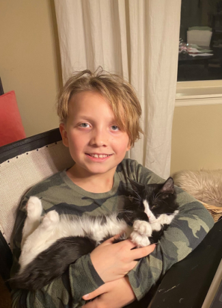 A boy smiling and holding a black and white cat