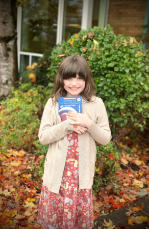 A girl holding a book outside.