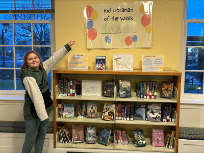 Cora proudly gesturing to her Kid Librarian display.